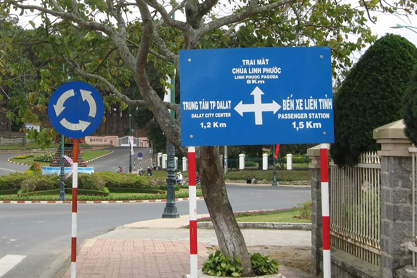 Biển chỉ hướng nền xanh ở Đà Lạt chỉ ba hướng: Trại Mát, chùa Linh Phước 8 km; trung tâm thành phố 1,2 km; bến xe liên tỉnh 1,5 km, có dòng tiếng Anh; bên trái là biển tròn xanh vòng xuyến
